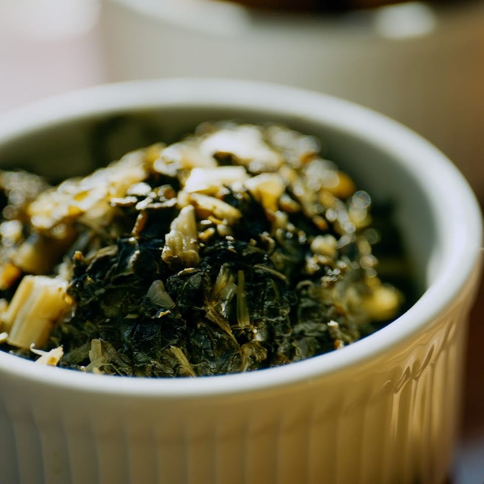 Close-up of a white ceramic bowl filled with cooked leafy greens and chopped vegetables on a restaurant table.