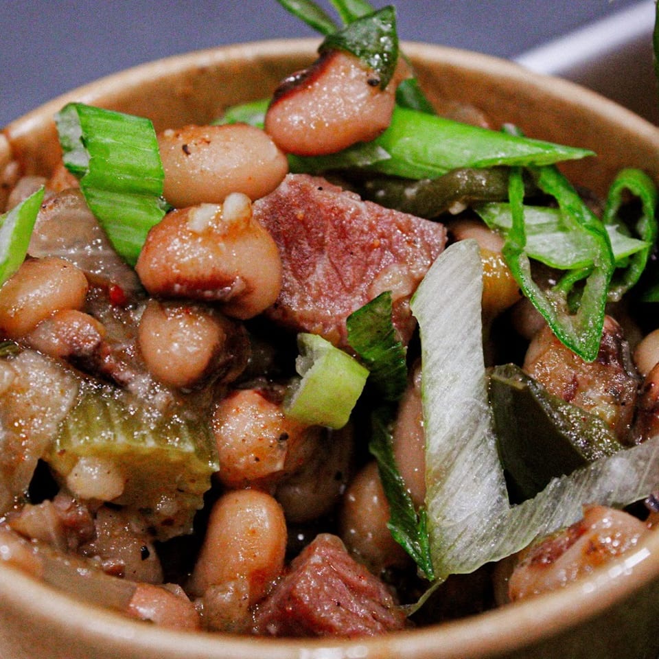 Close-up of a bowl filled with roasted meat, beans, peppers, and fresh green herbs.