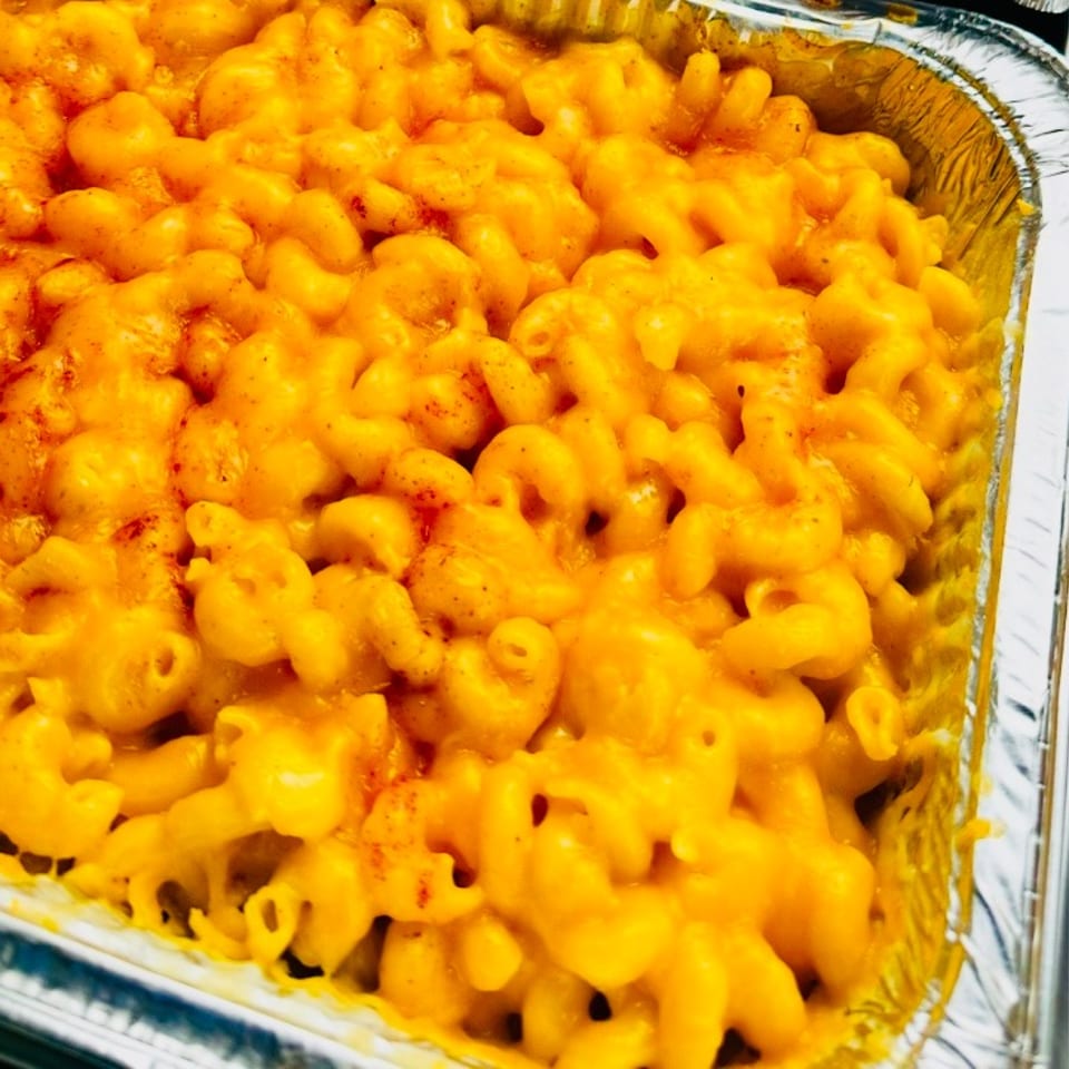 Close-up of creamy baked macaroni and cheese topped with melted cheddar and a light sprinkling of paprika in a foil tray.