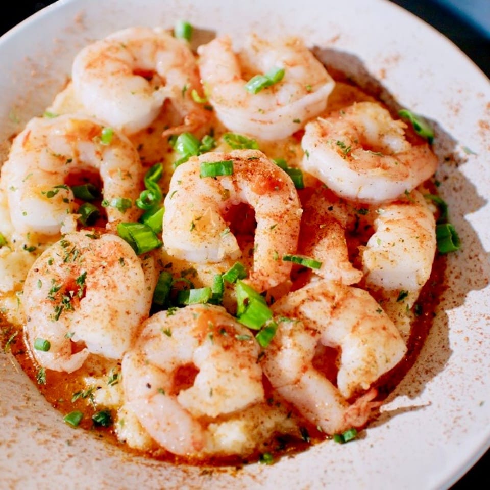 Seasoned shrimp garnished with chopped green onions, served in sauce on a white plate.