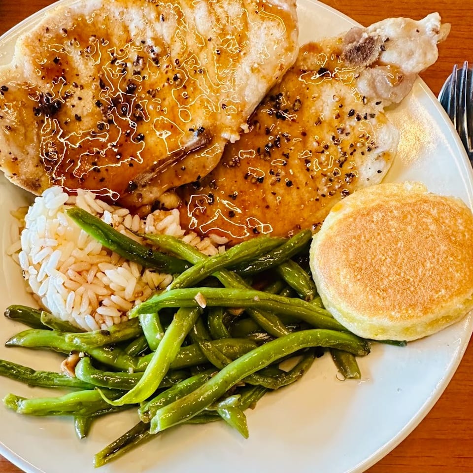 Plate of glazed grilled chicken, rice, green beans, and a golden biscuit on a restaurant table.